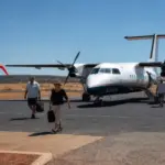 Passengers walking toward a small propeller aircraft on a regional airstrip